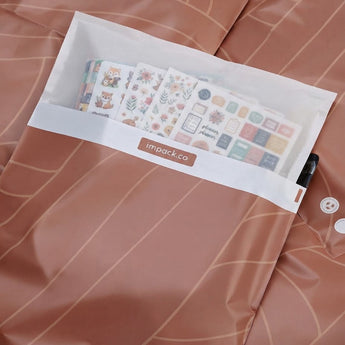 A transparent pocket on a brown patterned surface holds several sticker sheets featuring animals, plants, and icons. The pocket is labeled “impack.co.”.