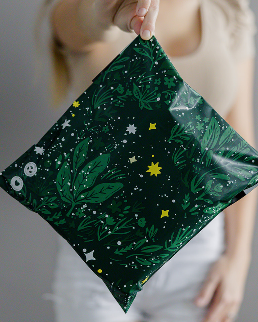 A person holds out a green, square-shaped package decorated with leafy and star patterns.
