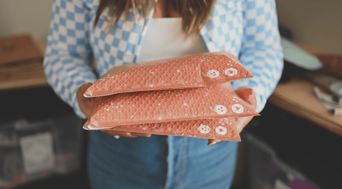 A person holds three padded mailers.