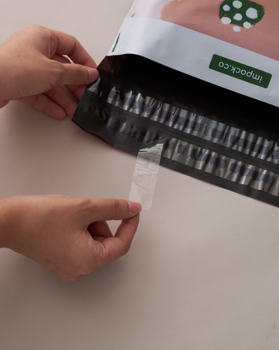 A person peels a clear strip from the seal of a black and pink plastic food package labeled "Impac+Co.