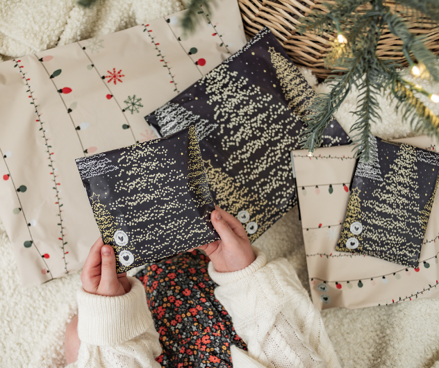 Child holding a wrapped gift with starry night design, surrounded by more decorated presents under a pine branch.