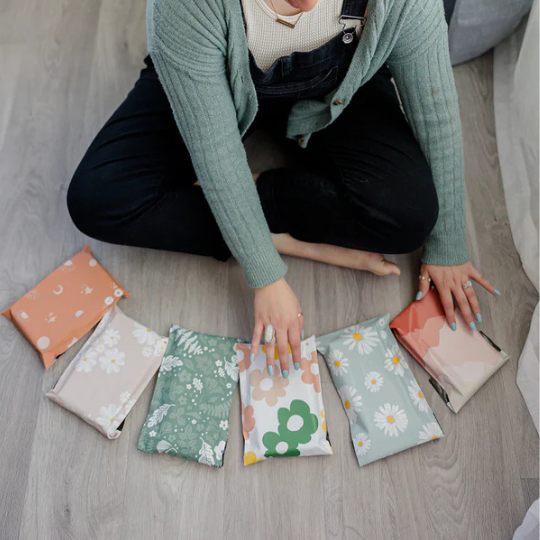 Person sitting cross-legged on the floor, arranging seven patterned fabric pouches in a semi-circle on wood flooring.