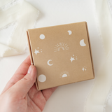 A hand holding a small impack.co ABC Box Celestial 4" x 4".