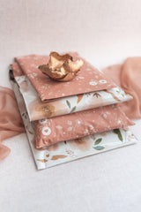 Three impack.co SALE Floral 2D Rosy Brown Biodegradable Mailers (10" x 13") are stacked on a light surface, showcasing eco-friendly, stylish packaging and reliable protection, topped with a decorative gold ceramic dish.