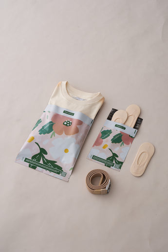 A floral shirt in a clear bag is paired with a pastel package containing insoles, a beige belt, and nude no-show socks on a light background. Perfectly packaged in impack.co's SALE - Pastel Petals Mailers 10" x 13" for optimal transit protection.