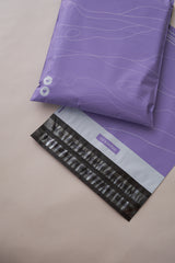 Two Tidal Lilac Mailers (10" x 13") by impack.co, featuring a wavy line design, sit on a beige background. One is partially open, showing a striped black and gray interior ideal for versatile packaging and transit protection.