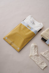 A white t-shirt, beige knit hat, and socks rest on a light surface. These items arrive in impack.co's SALE - Tidal Amber Mailers (10" x 13"), an eco-friendly choice for stylish, medium-sized shipments with yellow packaging.