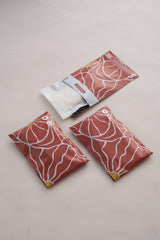 Three artistic pouches, patterned in red and white like the SALE - Crimson Grove Mailers by impack.co, rest on a light surface. One is partially open, revealing its contents.