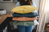 A woman holding a stack of Space Blue Leaf Biodegradable Mailers 14.5" x 19" by impack.co in front of a desk.