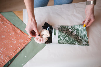A woman is putting an Emerald Evergreen Biodegradable Mailers 6" x 9" from impack.co into a bag.