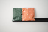 The black shelf holds two colorful bags: "SALE - Olive Leaf Biodegradable Mailers" by impack.co, with green leaves and orange celestial patterns. These versatile packaging solutions offer style while ensuring transit protection for your cherished items.