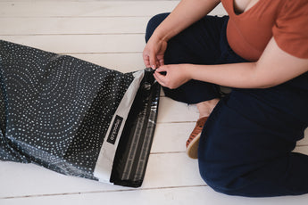 A woman is putting a recyclable Wavy Dots Biodegradable Mailers 19" x 24" bag from impack.co on the floor.