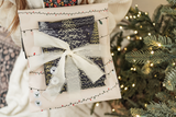A SALE item from impack.co features Christmas Tree Biodegradable Mailers (10" x 13") with holiday-themed designs and ribbon bows, perfect for gifting near a festive Christmas tree.