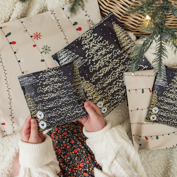 A child holds an impack.co SALE - Christmas Light Strings Biodegradable Mailer (10" x 13"), surrounded by festive packaging and a pine branch—perfect for sending medium-sized holiday gifts sustainably.