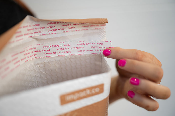 A person with pink nail polish seals an impack.co SALE - Celestial Tan Biodegradable Bubble Mailer (8.5" x 12") by peeling adhesive strips.