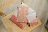 Four Mountain Clay mailers (impack.co) in pink and white rest snugly wrapped on a wooden chair with a woven seat.