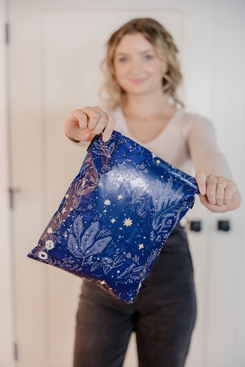 An individual is indoors holding an impack.co SALE - Midnight Indigo Mailer, 10" x 13", featuring a blue star pattern for transit protection.