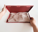 A person opening an impack.co SlimBox with an ABC Box Cedar Leaf 9.8" x 13.3" - Extra Large sweater inside.