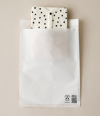 A white, partially transparent plastic packaging bag with recycling symbols and text on the front. A polka-dot fabric item is partially visible inside the impack.co Glassine Bags 9.6" x 12.6", protruding from the top.