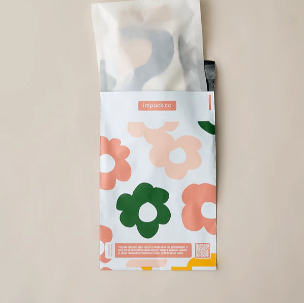 A partially opened floral-patterned mailing bag with pink and green flowers on a beige background, revealing contents inside.