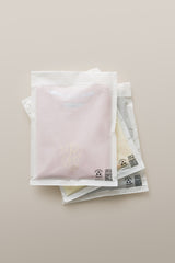 Three folded t-shirts in transparent, resealable impack.co Glassine Bags 9.6" x 12.6" with visible QR codes on a neutral background.
