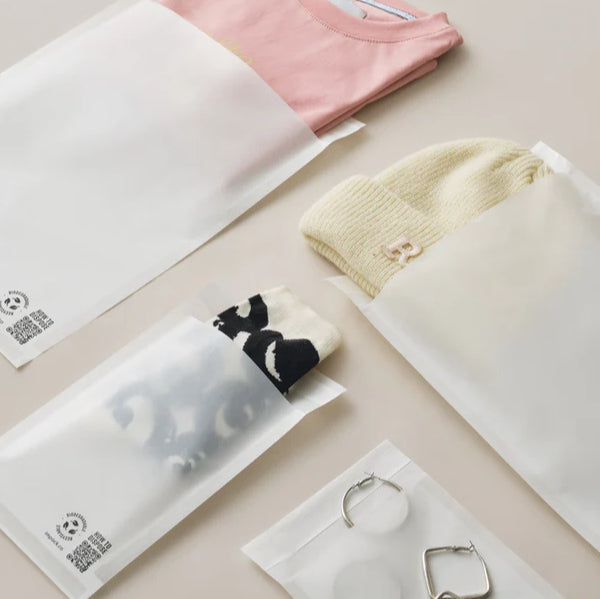 Four translucent paper bags contain folded clothing, a pair of socks, and hoop earrings, displayed on a light-colored surface.