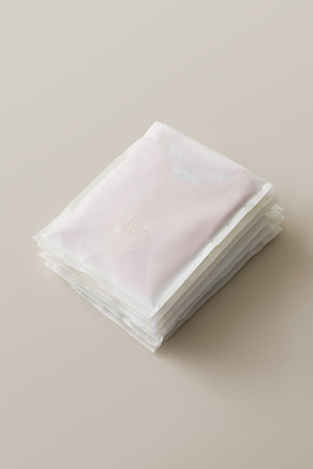 A stack of neatly folded pastel-colored t-shirts is individually packaged in impack.co Glassine Bags 9.6" x 12.6" on a light background.