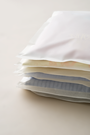 Glassine Bags 9.6" x 12.6" by impack.co containing folded clothes stacked on a flat surface.