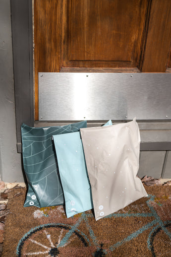 A Space Blue Leaf Biodegradable Mailers 14.5" x 19" from impack.co sits on a rug in front of a door, ready for shipping.