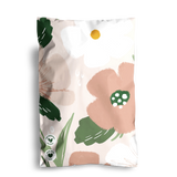 A floral-patterned packaging with large flowers in pink, green, and white hues. The Large Flowers Mailers 6" x 9" by impack.co are designed for storing small accessories and feature green certification stamps at the bottom left corner.