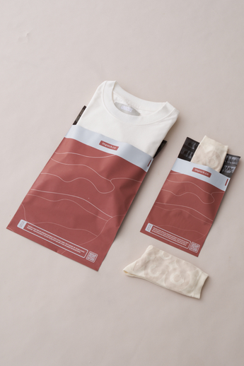 A folded white t-shirt and socks rest stylishly beside their reddish-brown impack.co SALE - Tidal Terracotta Mailers 6" x 9" on a light surface, highlighting the blend of style and sustainability with biodegradable packaging for eco-friendly shipping.