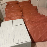 The bed is adorned with stacks of orange padded envelopes and white boxes labeled "FOR YOU," all showcasing a subtle cedar leaf print. The impack.co's SALE - Natural Cedar Leaf Biodegradable Mailers, measuring 14.5" x 19", add a touch of eco-friendly style with their durable construction.