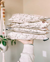 A hand holds a stack of four Wildflower Biodegradable Mailers by impack.co, exuding rustic charm against a neutral background.