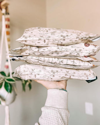 A hand holds a stack of four Wildflower Biodegradable Mailers by impack.co, exuding rustic charm against a neutral background.