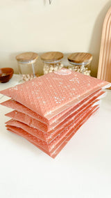 A stack of Rosy Brown Biodegradable Bubble Mailers 6" x 9" from impack.co sitting on a counter.