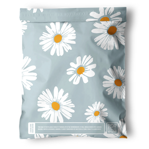 The Daisy White Biodegradable Mailers 10" x 13" by impack.co come in a light blue resealable bag with white daisies and yellow centers, designed for eco-friendly shipping with a barcode, QR code, and recycling message at the bottom.