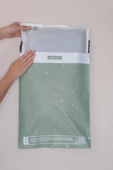 Hands gently place an item into a glassine bag labeled "impack.co," featuring decorative white dots, perfect for garment packaging.