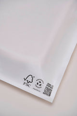 Close-up of a Glassine Bag by impack.co, measuring 14.1" x 18.6". This white biodegradable envelope is perfect for shipping t-shirts and features FSC and recycling symbols with a QR code in the bottom right corner on a plain background.