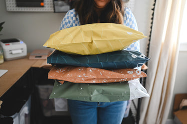 A woman holding a stack of pillows in her Mustard Leaf Biodegradable Mailers 14.5" x 19" office by impack.co.