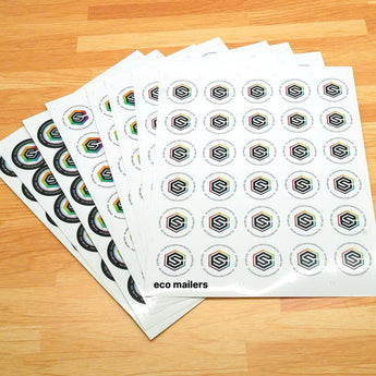 Sheets of impack.co's Custom Paper Sticker Sheets, showcasing a hexagonal design with "eco mailers" text, printed on uncoated paper stickers, beautifully arranged on a wooden surface.