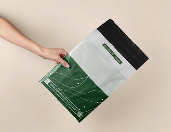 A hand holds the versatile, eco-friendly SALE - Japanese Green Mailers 10" x 13" by impack.co against a beige background, highlighting biodegradable mailers that ensure reliable transit protection.