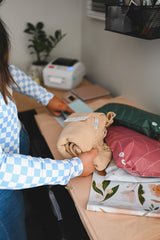 A woman is putting Olive Leaf Biodegradable Mailers 14.5" x 19" from impack.co on a table.