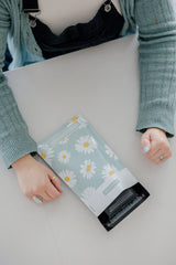 A person in a green sweater and overalls places their hands on a white table beside an impack.co SALE - Daisy White Biodegradable Mailer, showcasing their interest in sustainable packaging solutions.