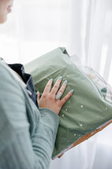 A person clutches a SALE - Starry Lily Pad Biodegradable Mailer by impack.co with one hand; their fingernails are painted blue, and they wear a ring.