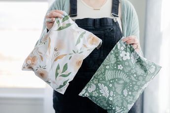 A woman is holding up two Biodegradable Mailer 10" x 13"" bags with floral prints on them from impack.co.