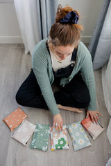 Seated on the floor, someone arranges a row of colorful SALE - Mountain Clay Mailers (6" x 9" CA) by impack.co, ideal for sustainable shipping and transit protection.