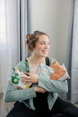 The person sits smiling and looking to the side, holding several colorful impack.co biodegradable mailers adorned with daisy and cosmos prints.