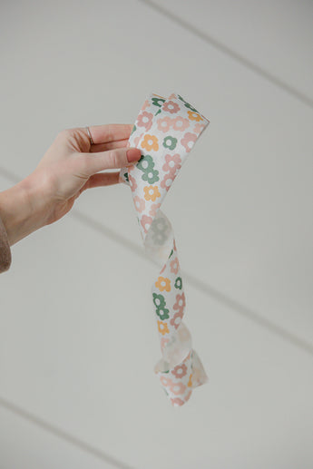 A hand holds a spiraled ribbon of impack.co's SALE - Packing Tape, showcasing the Daisy Multi print in pink, green, and yellow against a white background.