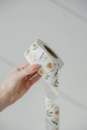 A person holding a roll of Packing Tape - Camelia Bloom from impack.co with a floral pattern.