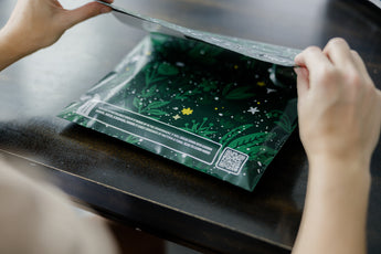 A woman folding up a Midnight Lush Mailers 14.5" x 19" from impack.co on a table.